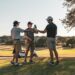 Tre golfspillere skåler sammen på en golfbane ved en golfvogn