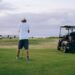 Golfspiller venter på banen ved siden af en golfvogn med udstyr