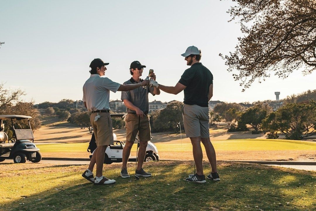Tre golfspillere skåler sammen ved golfbanen med golfvogne i baggrunden