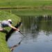 Golfspiller henter en bold i et vandfyldt strafområde ved banen
