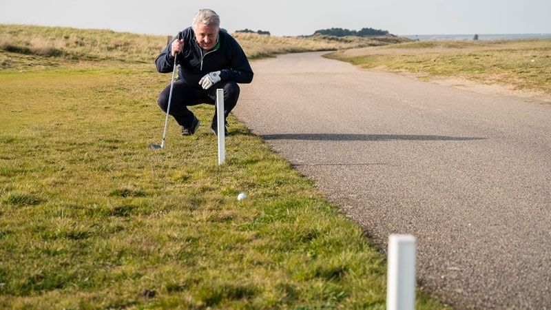 Golfspiller undersøger en golfbold nær en hvid banemarkering